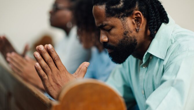 Black man praying with family in church pew